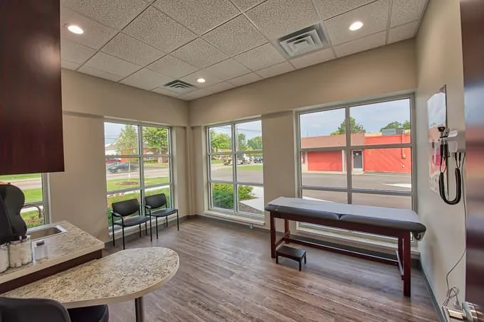 Bright corner exam room with exam table, guest chairs and tall windows at Allergy & Asthma Physicians of Commerce Township
